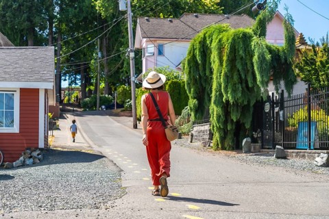 Tourist wearing a straw hat and orange jumpsuit walking along a yellow dotted line on a sunny