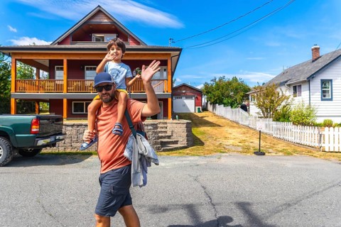 Father carrying his son on his shoulders waving in front of their house in chemainus, vancouver