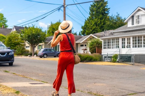 Tourist wearing a straw hat and red jumpsuit walking along a sunny sidewalk in chemainus, vancouver