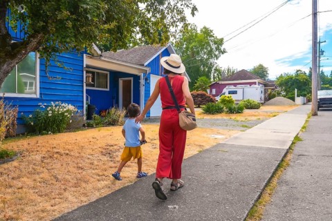 Mother and son walking away from a colorful blue house on a summer day in a residential