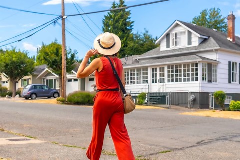 Female tourist wearing a straw hat and holding her hat while walking down a residential street in