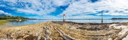 Rocky coastline stretches towards a red and white lighthouse, with sailboats dotting the tranquil
