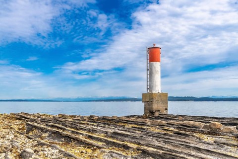 Red and white navigation marker stands on a rocky coastline in chemainus, british columbia, with
