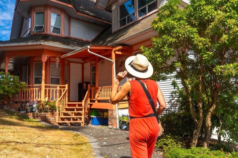 Female tourist wearing a straw hat and a red jumpsuit walking near a colorful wooden house in