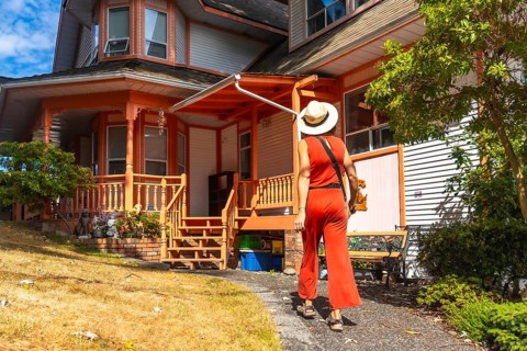 Tourist in a straw hat and red jumpsuit walking away from a colorful victorian house in chemainus,