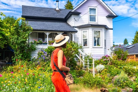 Tourist wearing a straw hat and orange dress walking through a colorful blooming garden in front of
