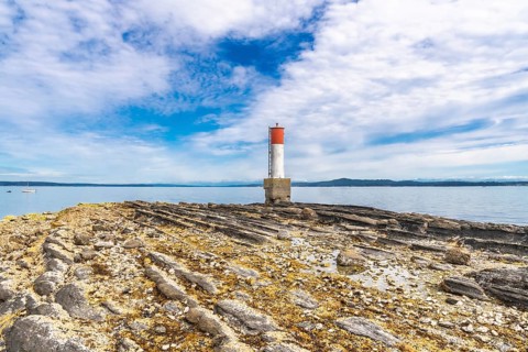 Red and white lighthouse rising from a rocky, textured coastline in chemainus, vancouver island,