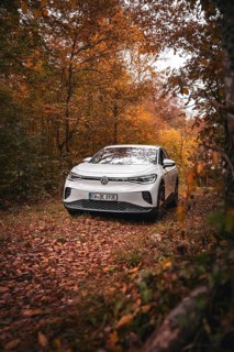 A white Volkswagen in the woods with warm autumn leaves, VW ID4 electric car, Deer Carsharing,