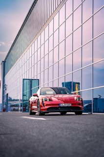Red car standing in front of a modern glass building, reflecting sky in the background, Porsche