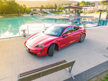 Red sports car next to a swimming pool and park bench in daylight, Porsche Taycan, Deer Carsharing,