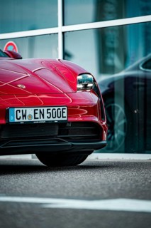 Partial view of the front of a modern red sports car in front of a glass façade, Porsche Taycan,