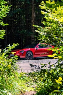 Red car in the forest surrounded by trees and shrubs, Porsche Taycan, deer car sharing. Calw,