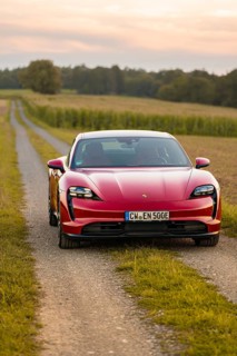 A red sports car on a gravel road through a rural area at sunset, Porsche Taycan, deer car sharing.