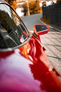 Red car with side mirror on a road with reflections, Porsche Taycan, Deer car sharing. Calw,