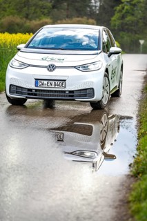 Car on wet road with clear reflection in the puddle, surrounded by green nature, ID3 VW, deer car