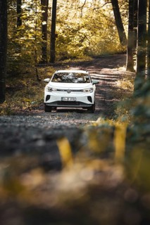 A car is parked on a forest path surrounded by autumn atmosphere and sun rays, VW ID4 electric car,