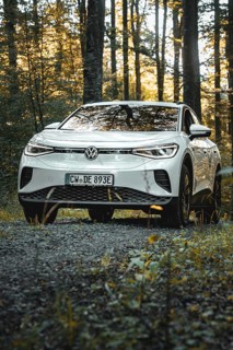 A white car is parked on a gravel path in the forest at dusk, VW ID4 electric car, Deer Carsharing,