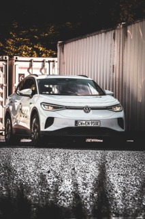 A car on a gravel field next to stacked containers in the shade, VW ID4 electric car, Deer
