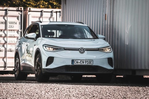 A white car is parked next to several containers on a gravel field, VW ID4 electric car, Deer