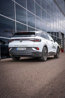 White car in front of glass façade on paved road, VW ID4 electric car, Deer Carsharing, Calw,