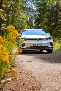 White Volkswagen on a forest road with yellow flowers in the foreground, VW ID4 electric car, Deer