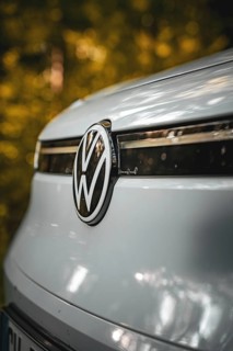 Close-up of VW logo on the front of a white car with forest in the background, VW ID4 electric car,