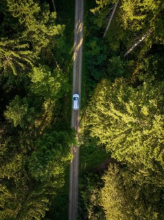 Drone shot of a car on a narrow forest path between trees, VW ID4 electric car, Deer Carsharing,