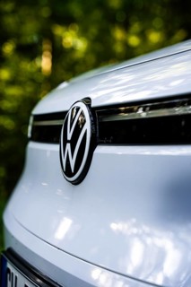 Close-up of VW logo on the front of a white car in the forest in daylight, VW ID4 electric car,