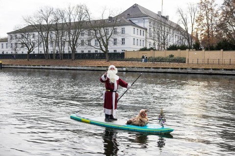 A water sports enthusiast dressed up as Santa Claus rides a SUP on the Spree in front of Bellevue