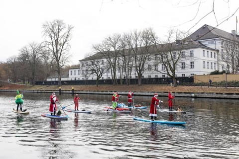 Water sports enthusiasts dressed up as Santa Claus ride SUPs on the Spree in front of Bellevue