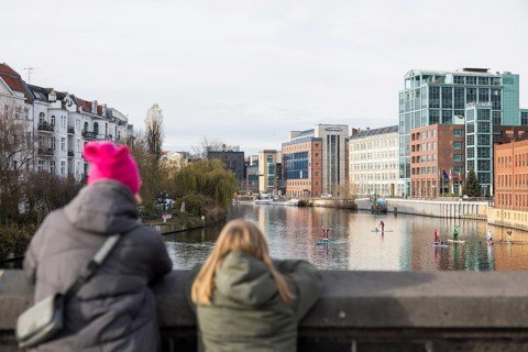 Passers-by watch water sports enthusiasts disguised as Santa Claus with SUPs on the Spree on the