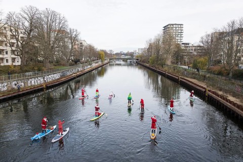 Water sports enthusiasts dressed up as Santa Claus ride SUPs on the Spree on the banks of the Hansa