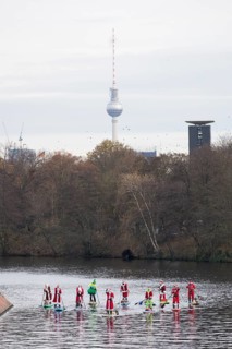 Water sports enthusiasts dressed up as Santa Claus ride SUPs on the Spree am Park at the