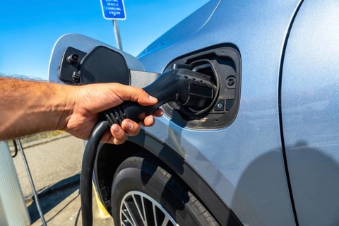 Hand inserting power cable into electric vehicle at a vehicle charging station, promoting