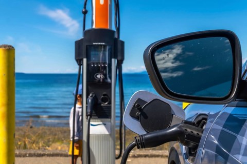 Modern electric vehicle connected to a charging station on the coast with a beautiful ocean view,