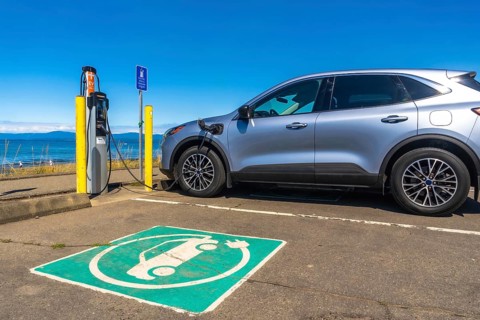 Silver electric car charging at a station by the sea, showcasing a picturesque ocean view while
