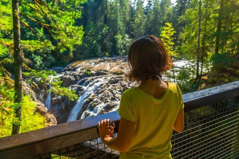 Female tourist standing on a viewpoint, admiring englishman river falls cascading through lush