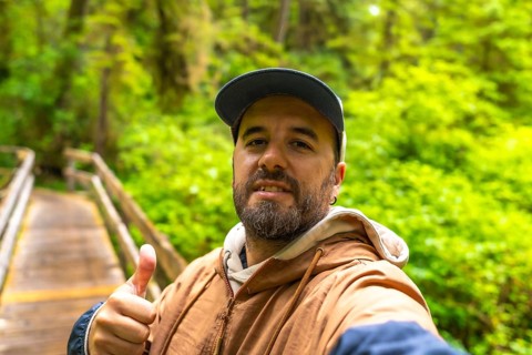 Tourist taking a selfie on a wooden boardwalk path, surrounded by lush rainforest vegetation,