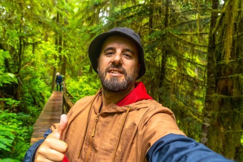 Happy tourist gesturing thumbs up while taking a selfie on a wooden walkway through a lush