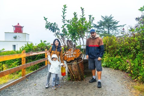 Happy family posing near the wild pacific trail sign with amphitrite point lighthouse in the