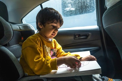 Young child concentrating on creating colorful artwork with crayons while secured in a car seat,