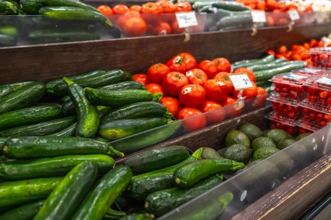 Wooden shelves displaying a variety of fresh produce including zucchini, tomatoes, cucumbers, and