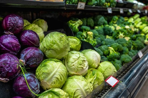 Fresh green and red cabbages and broccoli heads are neatly arranged on a refrigerated shelf in a