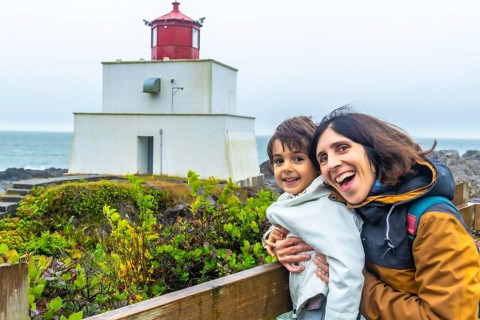 Happy mother and child hugging and smiling with the amphitrite point lighthouse in ucluelet,