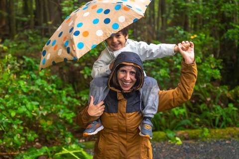 Happy mother giving piggyback ride to her smiling son under an umbrella while walking in a