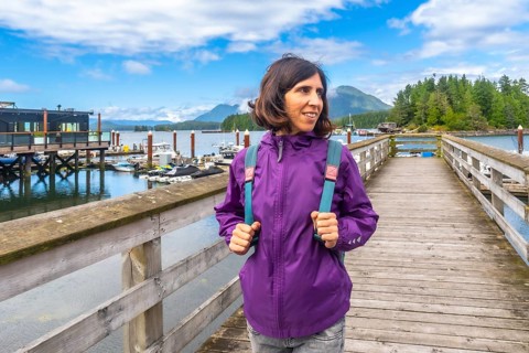 Female tourist wearing a purple jacket and carrying a backpack walking along a wooden pier in
