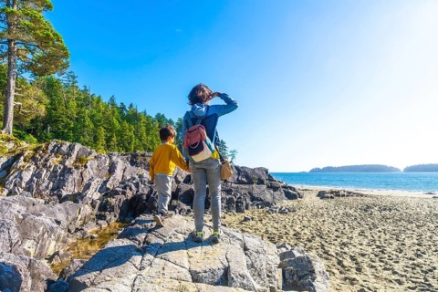 Mother and son holding hands. Exploring the beautiful rocky coastline near a sandy beach in tofino.