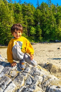 Young boy sitting on a large rock at a beach in tofino, british columbia, soaking up the summer sun