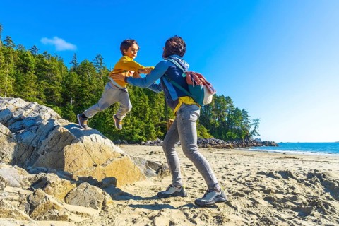 Mother catching her son as he joyfully jumps from a rock on a sandy beach, surrounded by lush green