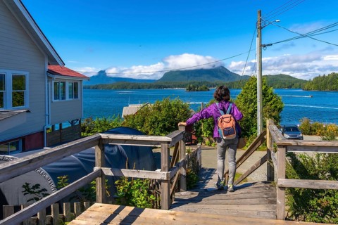 Female tourist with backpack walking down wooden stairs enjoying scenic view of tofino inlet,